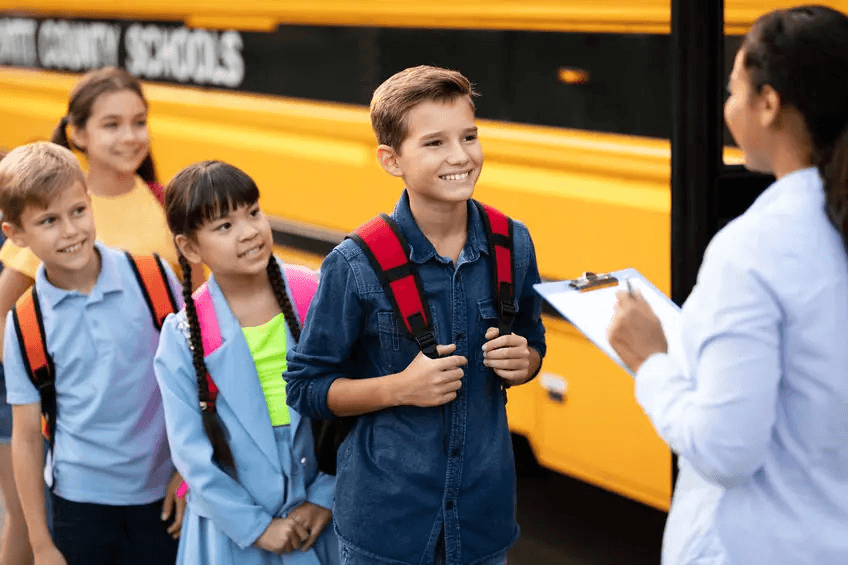 Smiling students with backpacks lining up to board a yellow school bus